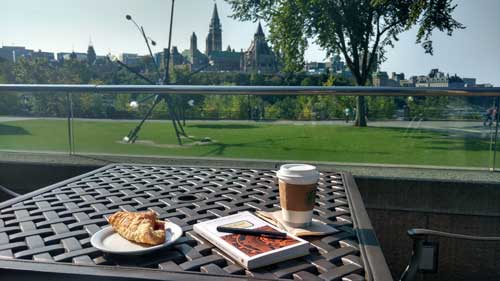 Book, coffee, and snack on a patio table overlooking the Parliament buildings in Ottawa